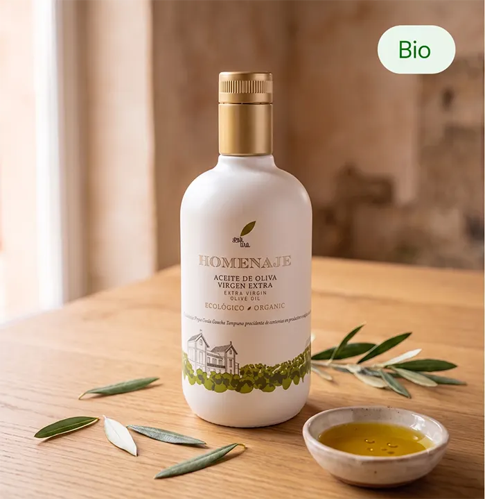 Bouteille d'huile d'olive vierge extra biologique Homenaje 500 ml posée sur une table en bois avec des feuilles d'olivier et un ramequin d'huile d'olive.